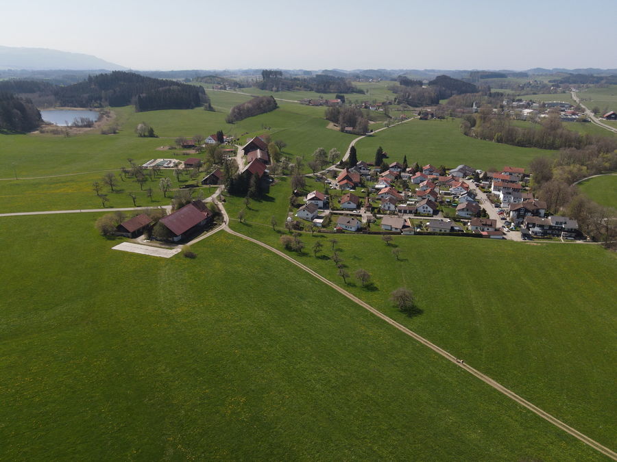 Grüne Wiesen und ein kleiner See am Rand einer Wohnsiedlung aus der Luft